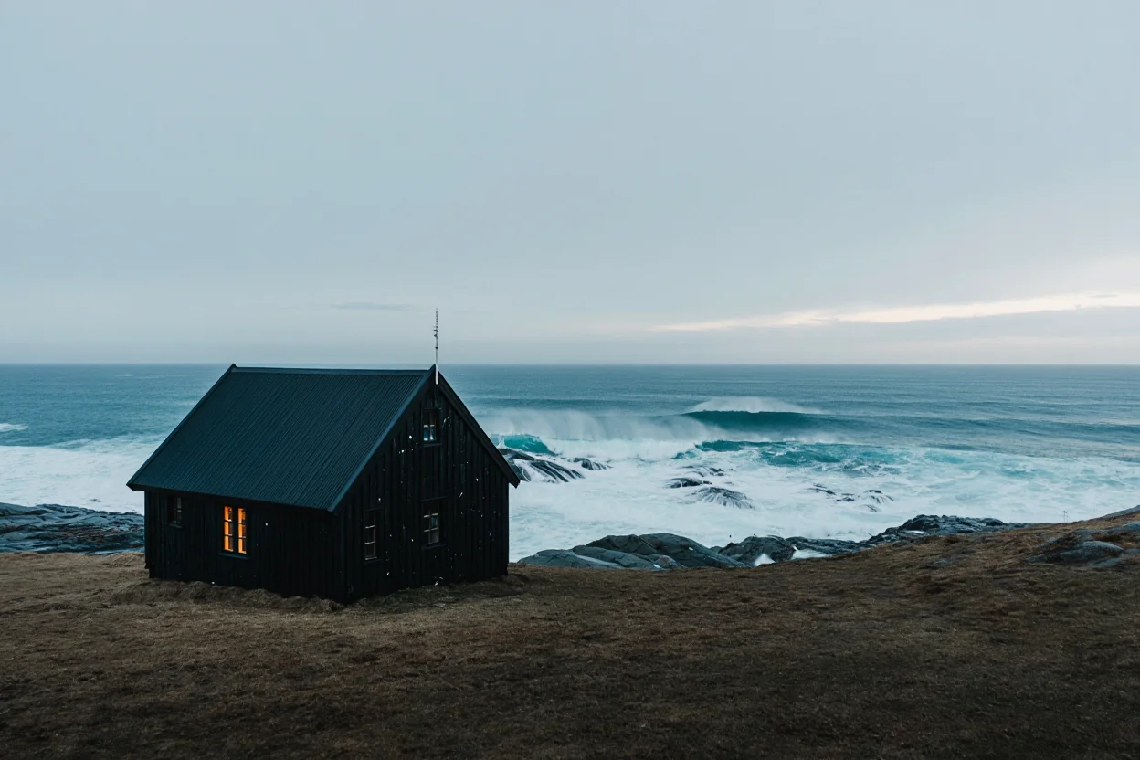 A solitary black wooden cabin, weathered by time, sits atop a windswept cliff overlooking a dramatic Nordic coastline. Waves crash against the rocks below, sending a fine mist into the air. The cabin, with its traditional green roof and warm glow emanating from its windows, provides a stark contrast against the steel-grey sky. The scene is captured in the style of a vintage Scandinavian travel poster, emphasizing the beauty of solitude and the ruggedness of the natural world.
