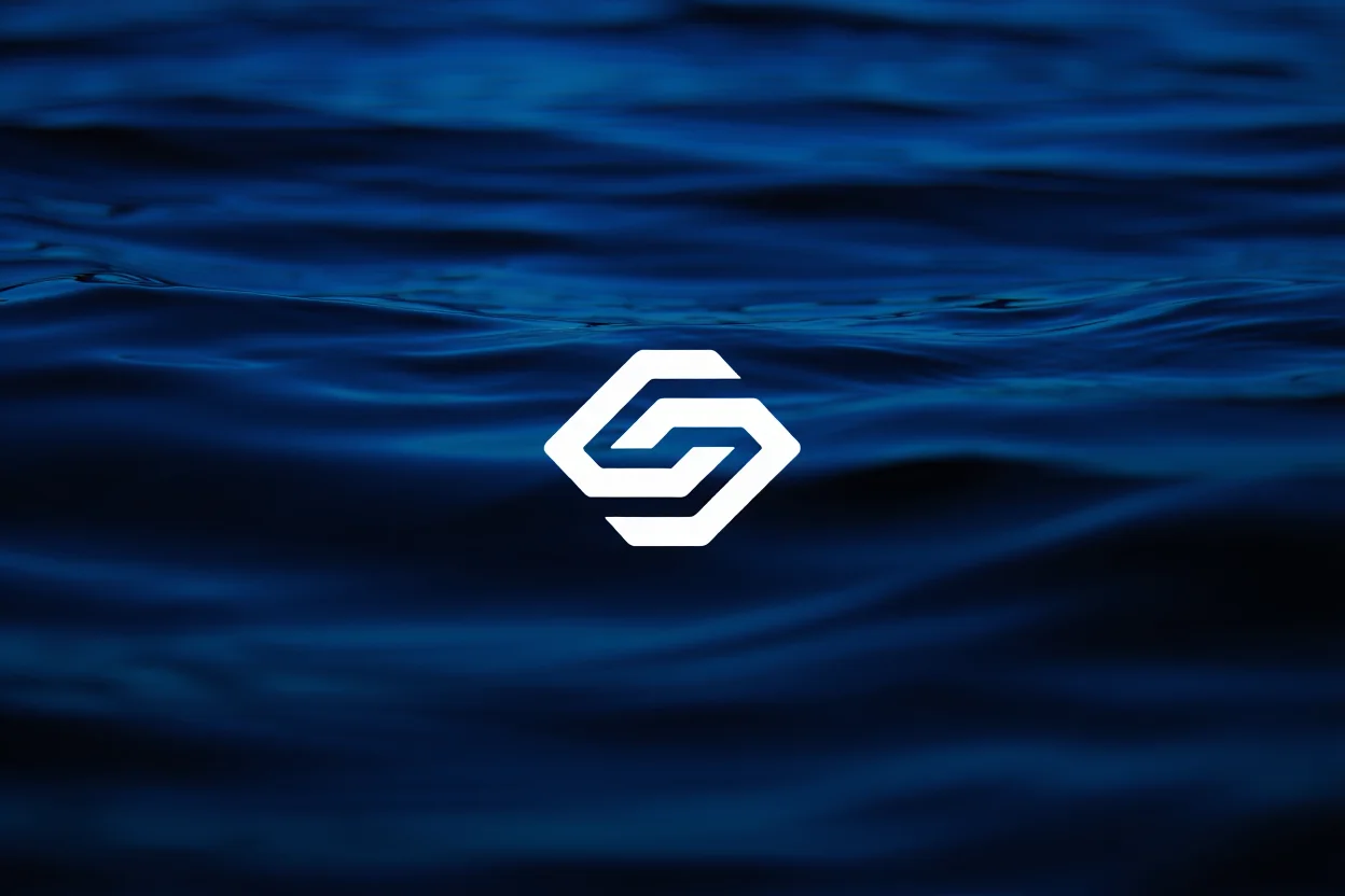 A dark blue underwater photograph showing variations in water depth captured through subtle gradients and textures. A centered white geometric logo spans the image horizontally, its edges crisp and well-defined against the deep marine blues of the background. Underwater photography with high contrast lighting and sharp focus on surface patterns.