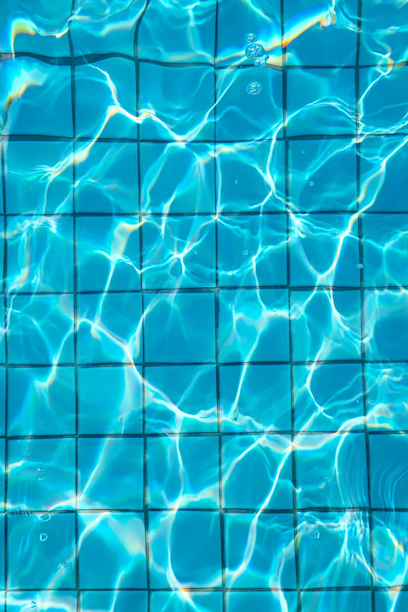 A pool scene captured from below the water's surface, looking up at a grid of light blue ceramic tiles. The tiles are distorted by rippling water, creating a wavy, refracted pattern characteristic of y2k-era digital aesthetics. Light streaming through the water casts shimmering cyan reflections across the tiles, while small air bubbles rise toward the surface. The underwater perspective emphasizes the geometric patterns of the square tiles arranged in neat rows and columns.  Digital photography with heavy color saturation and chromatic aberration effects typical of early 2000s editing techniques.